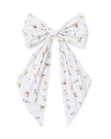 An Easter Basket and Wreath Bow in Easter Frolic with a large white bow featuring a pastel floral pattern is tied at the bottom of a wreath made of small white and pink flowers, hanging on a beige door.