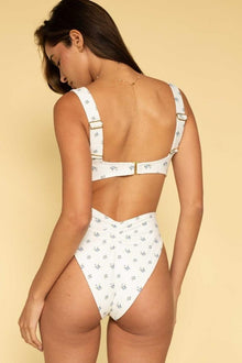 White bikini top with small blue floral print, adjustable straps, and gold buckle closure at center back.
