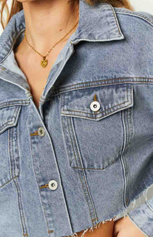 Side view of a mid-wash denim cropped jacket with a raw hem and button-front closure