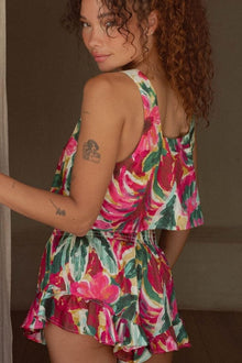 Woman wearing sleeveless tank top with pink, red, green and cream floral print and matching ruffled shorts.