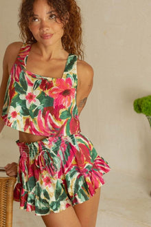 Woman wearing sleeveless crop top and matching short skirt in red, pink, yellow and green floral print with smocked waistband