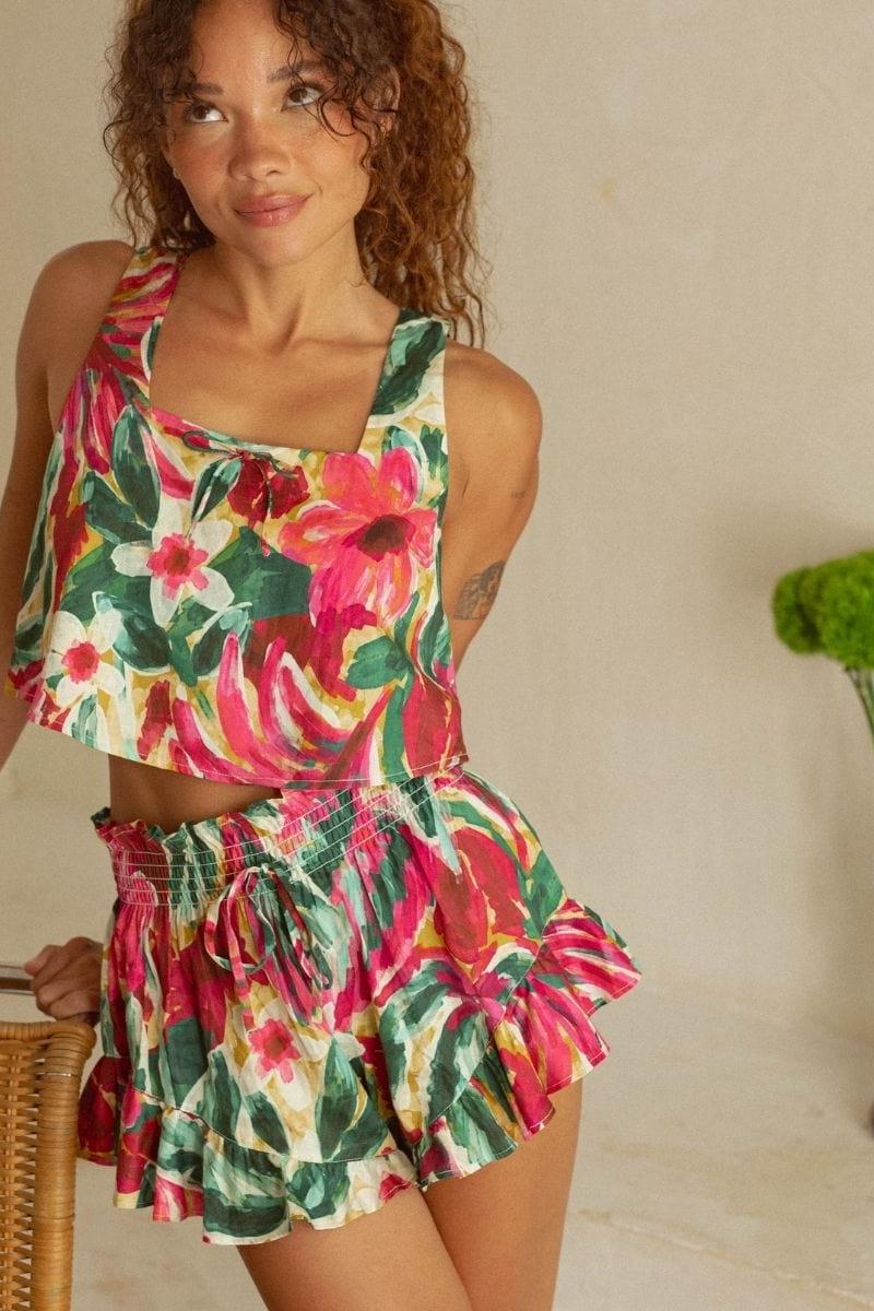 Woman wearing sleeveless crop top and matching short skirt in red, pink, yellow and green floral print with smocked waistband
