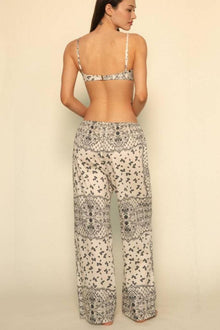 Woman wearing cream and black bandana-print wide-leg pants with drawstring waist and matching bikini top.