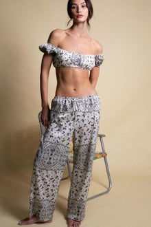 Woman wearing off-shoulder bandana print crop top and matching wide-leg drawstring pants with floral and geometric pattern.