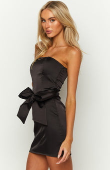 Side view of a black satin strapless mini dress with a large bow detail at the waist and side ruching