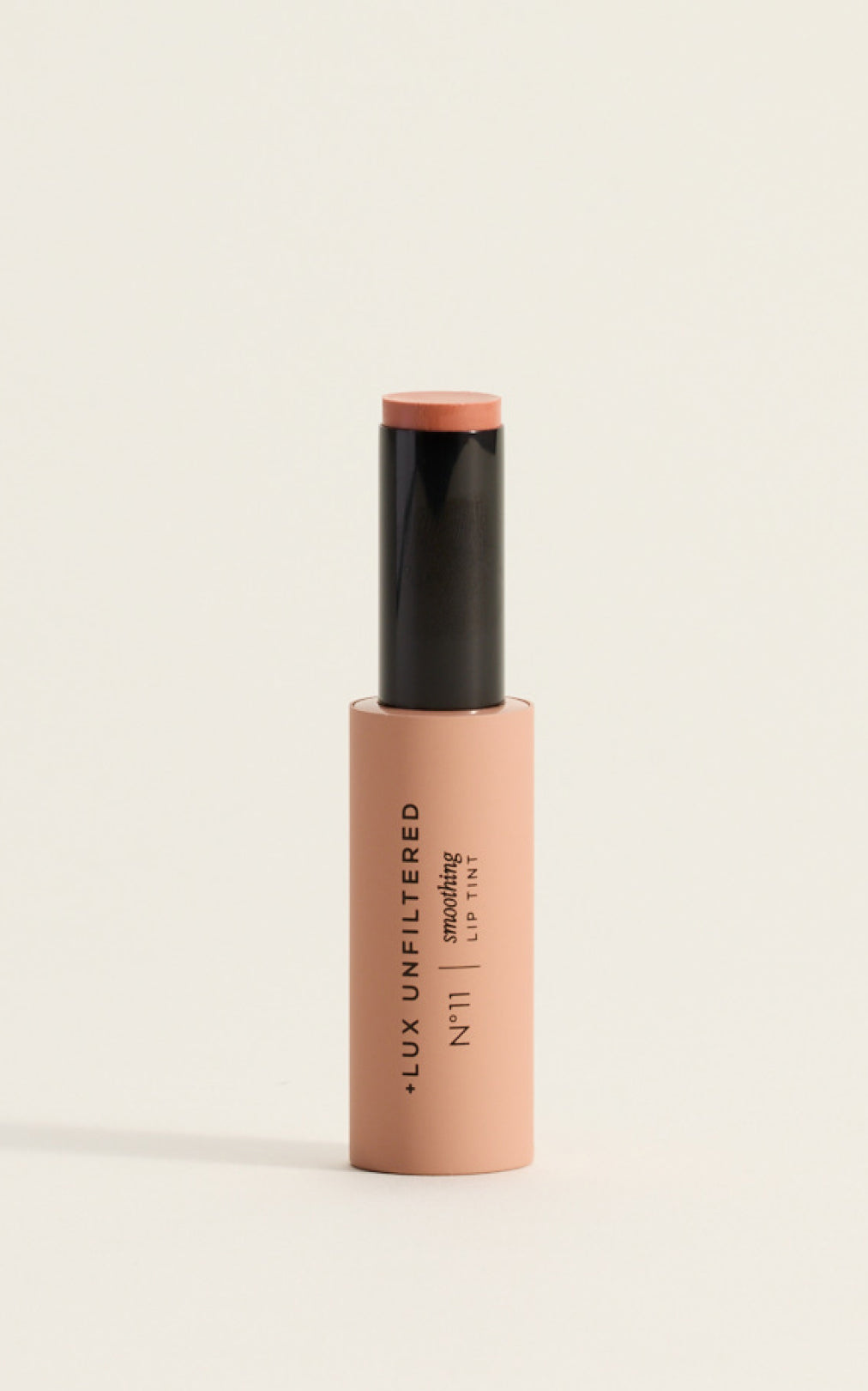 Close-up of Smoothing Lip Tint in Guava held by hand next to model's glossy coral-pink lips, showing creamy tint finish