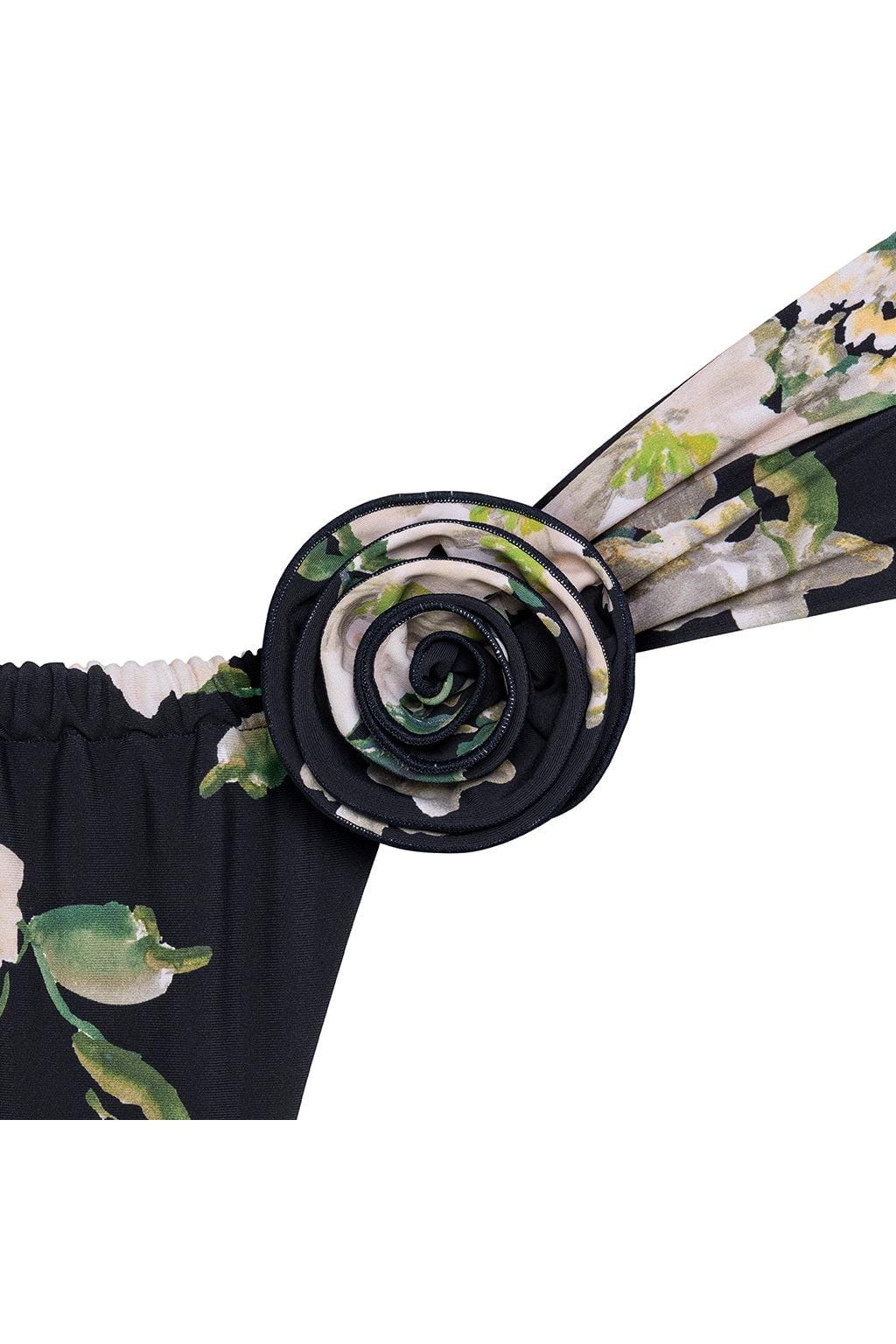 Layered rose-shaped pin in cream, black, and green tones attached to black fabric with floral pattern.