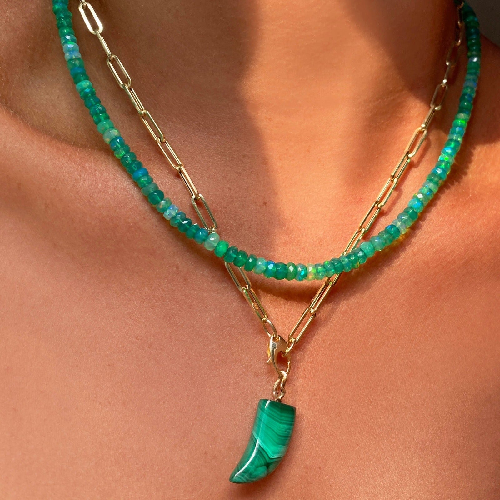 Shimmering beaded necklace made of faceted opals in shades of light green on a gold linking ovals clasp. Styled on a neck layered with the paperclip chain necklace and horn charm.