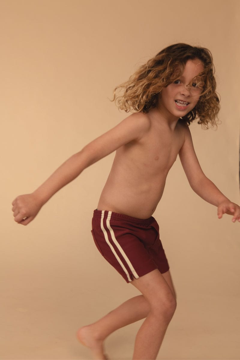 Maroon swim trunk with white side stripes on child model.