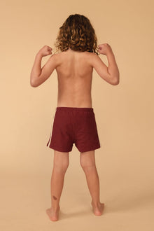 Child wearing maroon swim trunks with side stripe detail, shown from back view.
