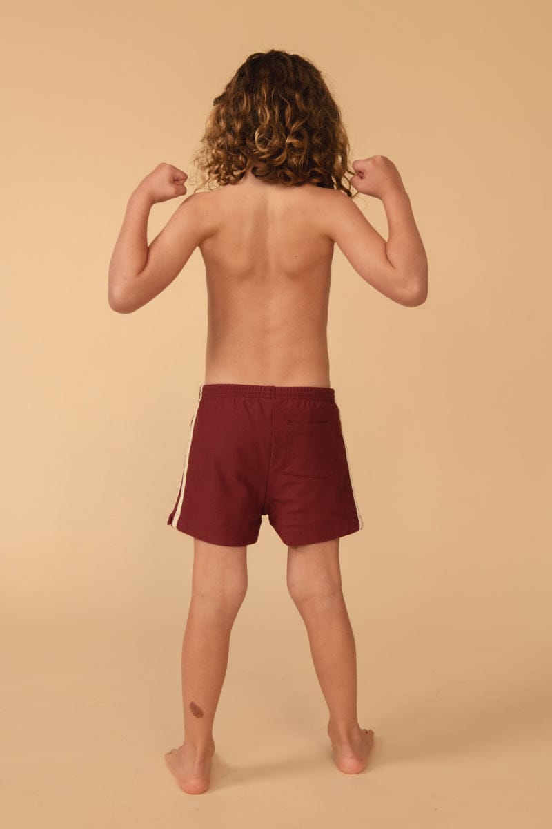 Child wearing maroon swim trunks with side stripe detail, shown from back view.