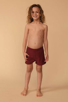 Child wearing maroon swim shorts with tan side stripes and drawstring waistband.