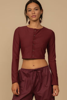 Maroon cropped cardigan with button front and long sleeves on model against tan background.