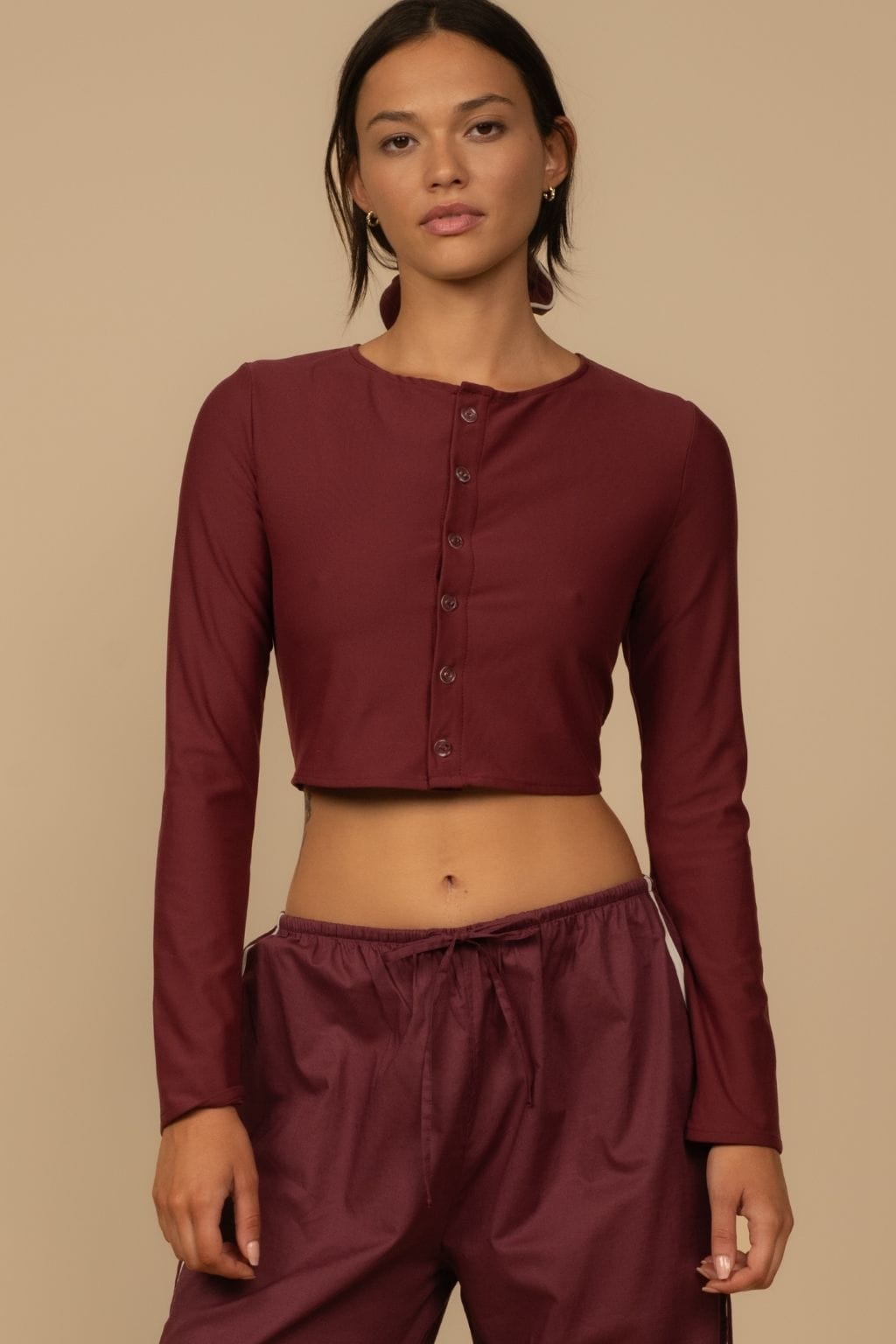 Maroon cropped cardigan with button front and long sleeves on model against tan background.