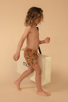 Child's swim trunk with multicolored floral print in red, yellow, and green on tan background.