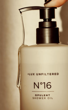 Close-up of Dripping In Opulence shower oil bottle showing black pump and oil dripping down against a beige background