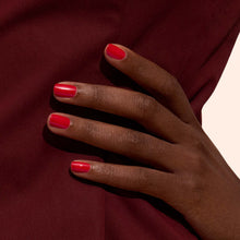 A hand with dark skin and neatly manicured nails painted in Manucurist’s Poppy Red rests against a burgundy fabric background.
