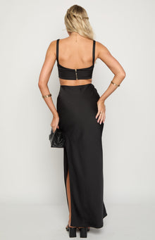 Rear view of a black formal maxi dress with an exposed gold zipper on the crop top and a high leg slit