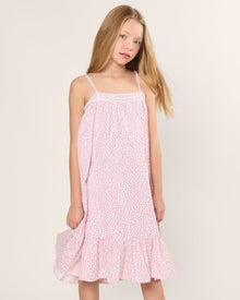 A young girl in a Girls Twill Lily Nightgown in Sweethearts by Petite Plume stands against a plain background. Her long blonde hair cascades freely, exuding relaxed comfort reminiscent of luxurious yarn-dyed cotton sleepwear.
