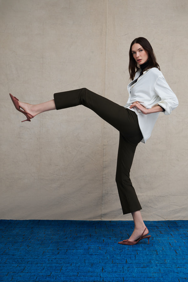 Woman wearing a white long sleeve button down and skinny black pants on a blue carpet floor and against a beige background | Exclude