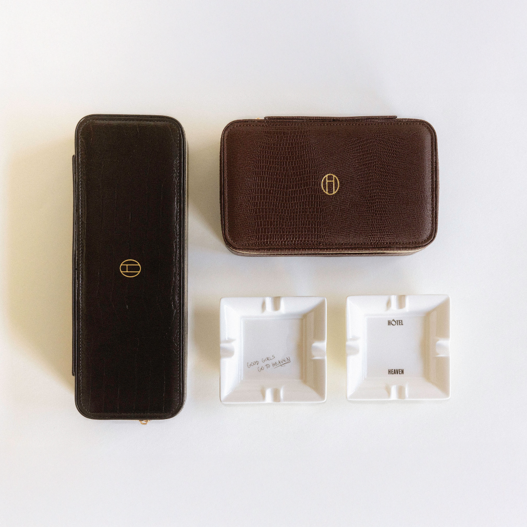 Two leather jewelry travel cases on a white background with two mini ashtrays that read (from left to right): Good Girls Go To Heaven and Hotel Heaven, respectively. 