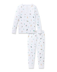 A young boy smiles, wearing the Petite Plume Kids Pima Snug Fit Pajama Set in Jingle Paws. This luxurious sleepwear features colorful small animal prints and provides comfort with its long sleeve top and pants as he stands barefoot against a plain background.