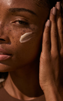 Close-up of freckled model with a dab of The Cleansing Balm on her cheek and her hand touching her face