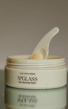 Close-up of open jar of The Cleansing Balm showing cream balm and spatula on a reflective surface