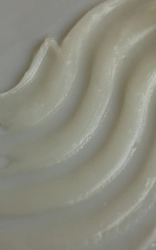 Close-up of The Cleansing Balm showcasing creamy white glossy balm texture with smooth ridges on a neutral background