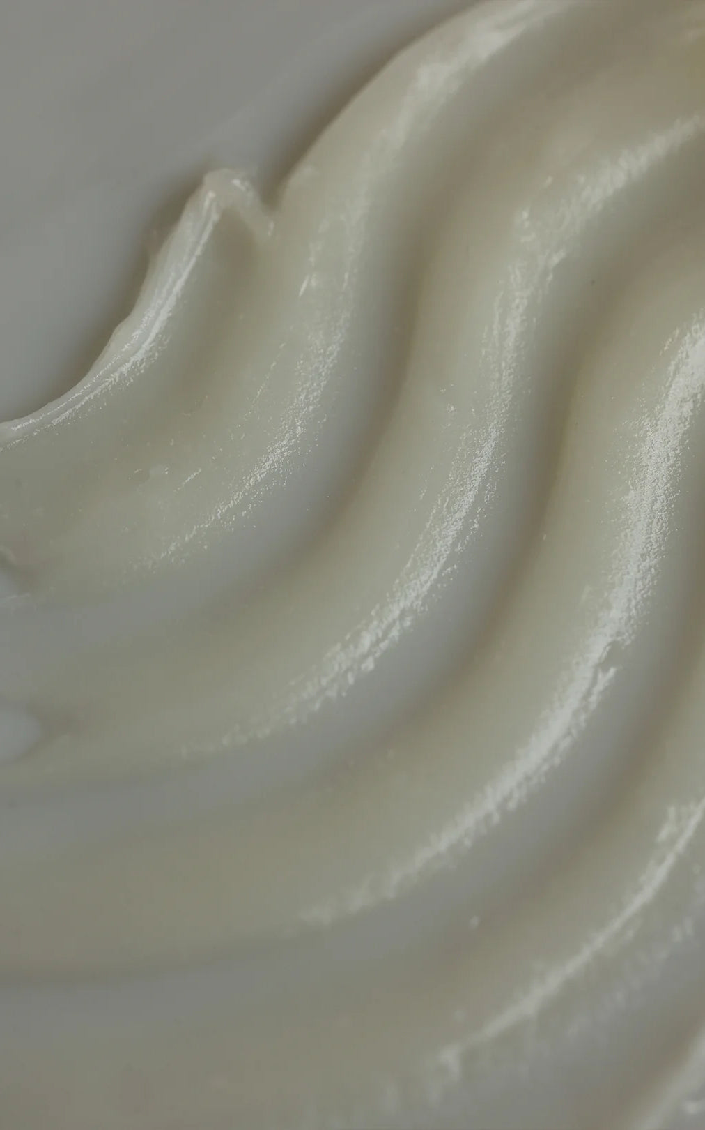 Close-up of The Cleansing Balm showcasing creamy white glossy balm texture with smooth ridges on a neutral background