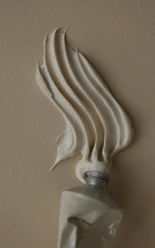 Close-up of The Polish tube showcasing beige cream fanned into textured ridges on a tan background