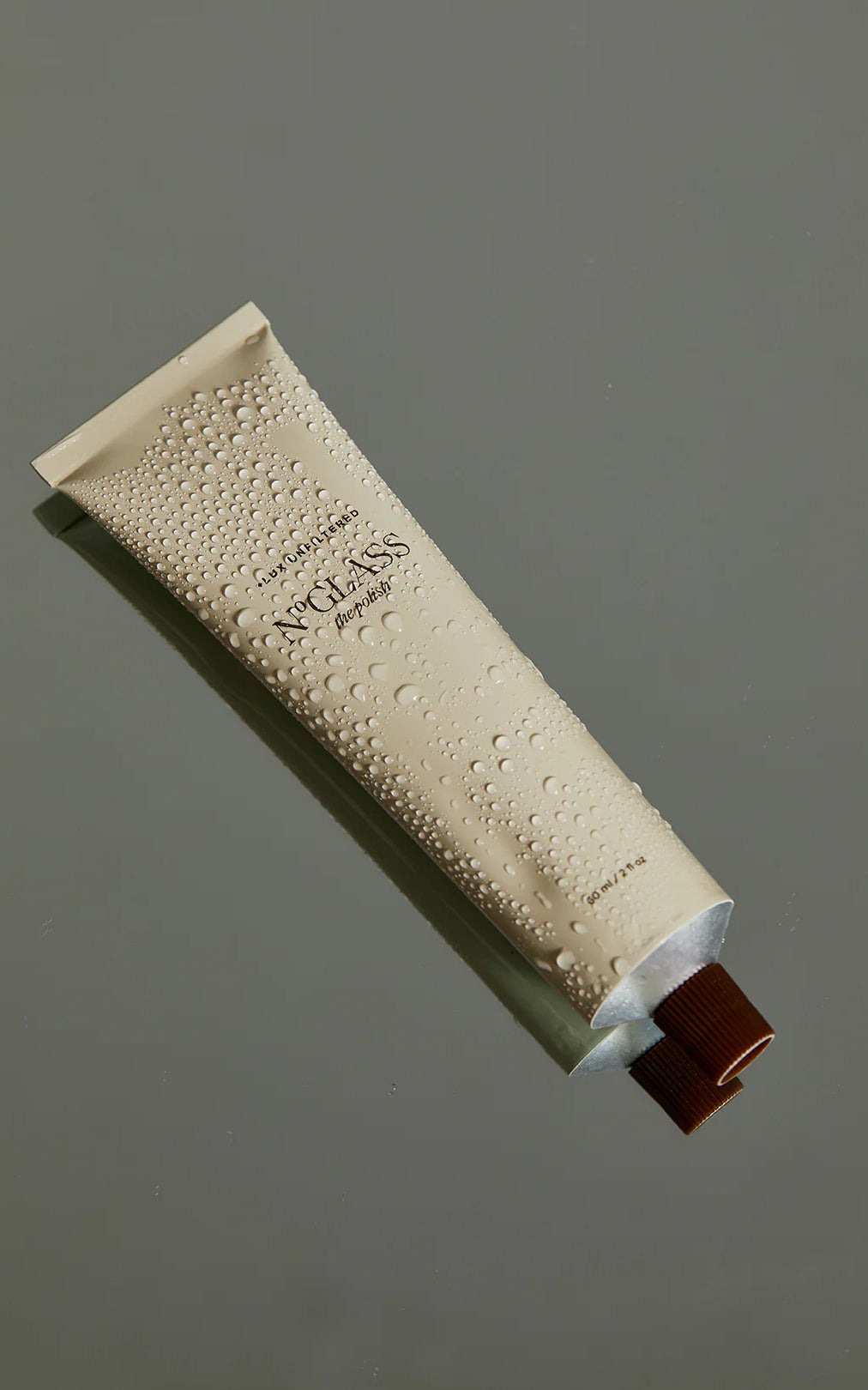 Beige tube labeled NOGLASS the polish and LUX UNFILTERED with water droplets and brown cap, 60 ml / 2 fl oz