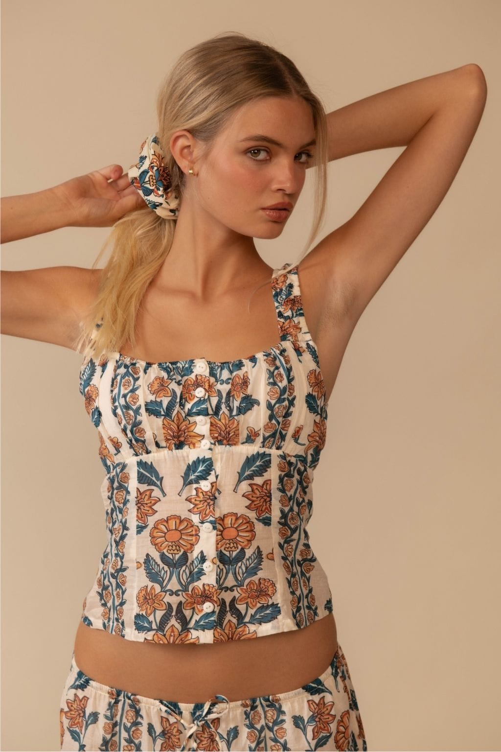Cream sleeveless tank top with orange and teal floral pattern, gathered neckline and ruched sides.