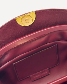 Close-up of a burgundy handbag with a gold clasp on a white background