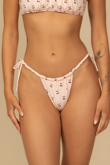 Pale pink scrunch bikini bottom with red cherry print and tie-side closures.