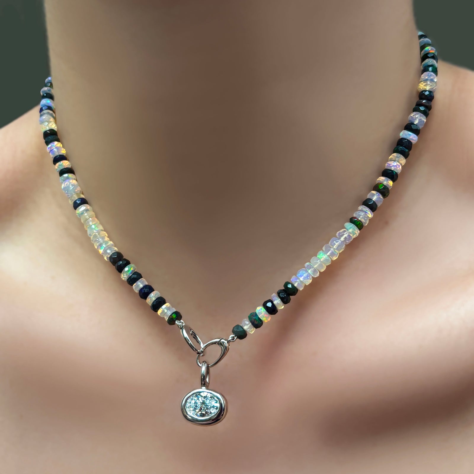 A small molten oval solitaire charm in the clasp of a double shade welo opal necklace on a model's neck.