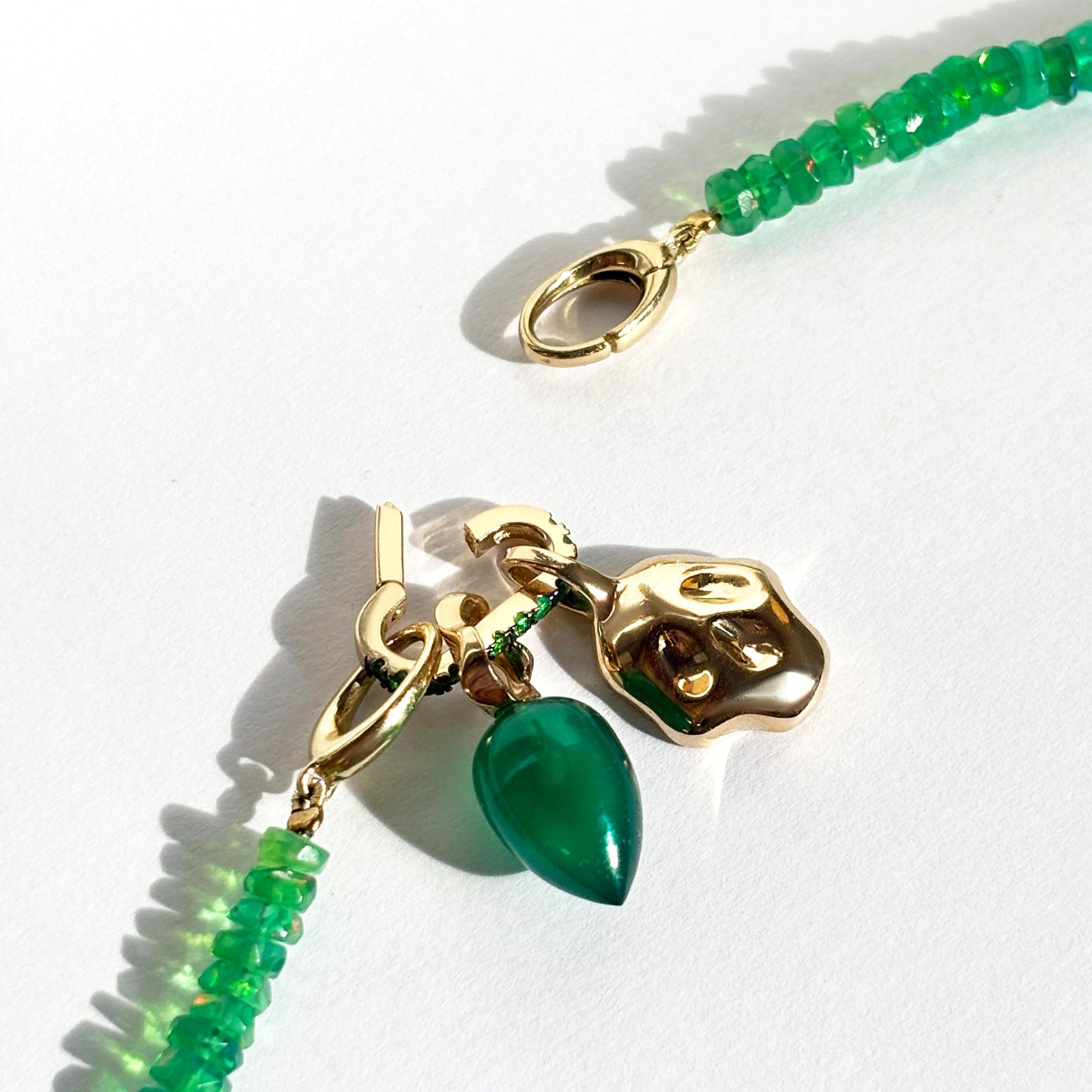 Green faceted opal necklace with molten skull charm, small emerald charm lock, and green onyx drop charm on a white background.