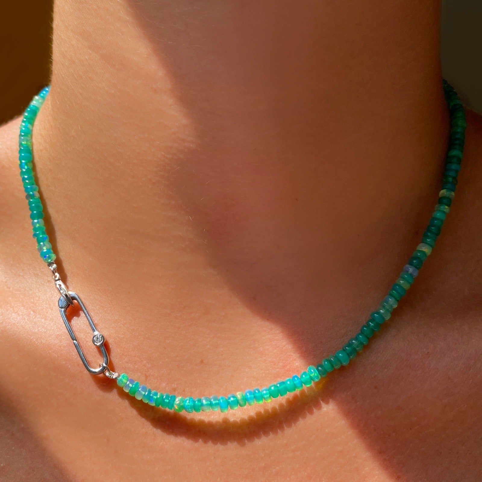 Shimmering beaded necklace made of faceted opals in shades of green on a gold linking ovals clasp. Styled on a neck layered with a paper clip charm lock.
