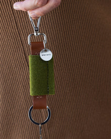 Woman holds green Merino Wool Bar Key Fob in one hand next to her side, close up