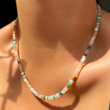 Shimmering beaded necklace made of smooth opal rondels in shades of tan, teal, orange and pink on a gold linking ovals clasp. Styled on a neck.