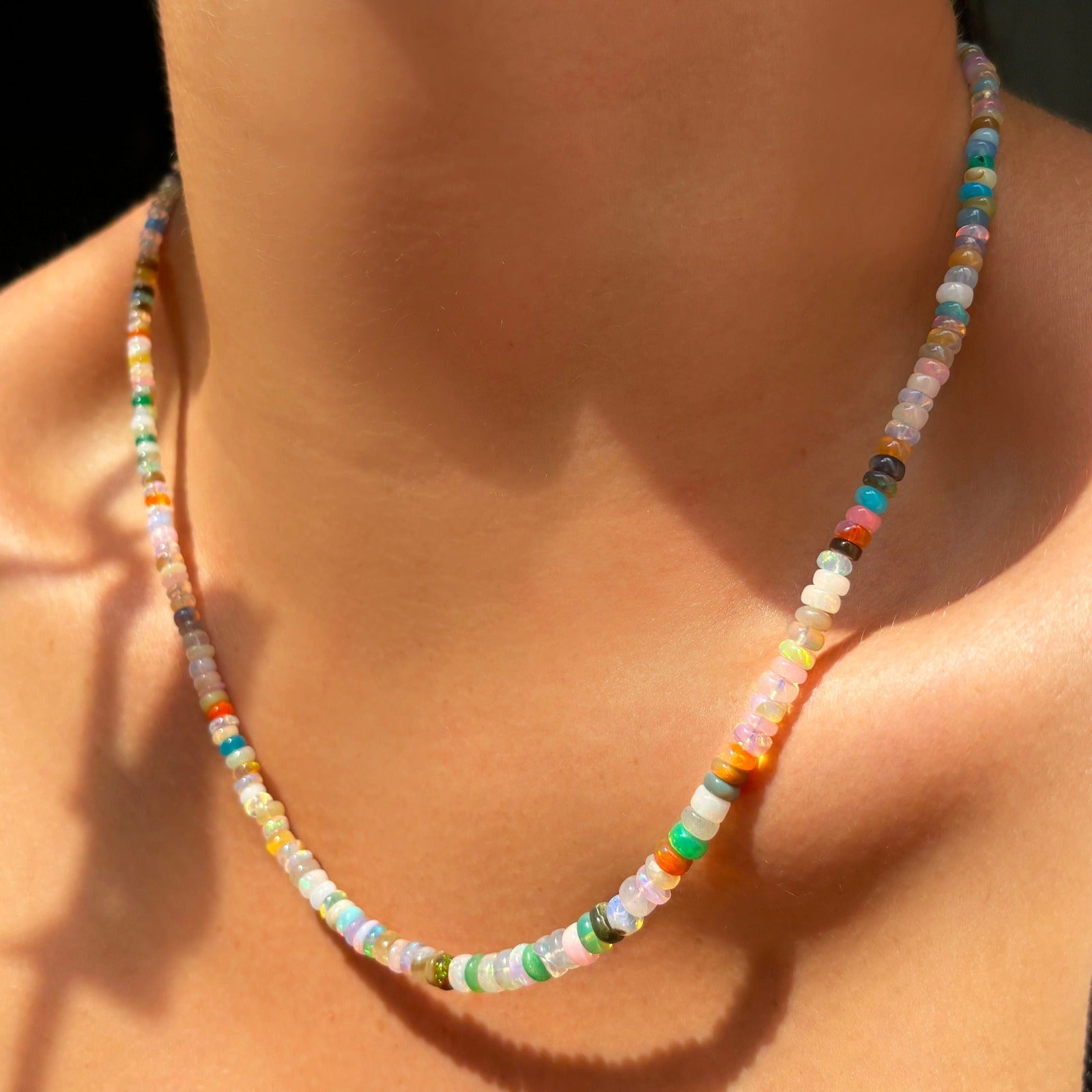 Shimmering beaded necklace made of smooth opal rondels in shades of tan, teal, orange and pink on a gold linking ovals clasp. Styled on a neck.