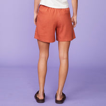 Back view of model wearing the linen pleated shorts in faded rust.