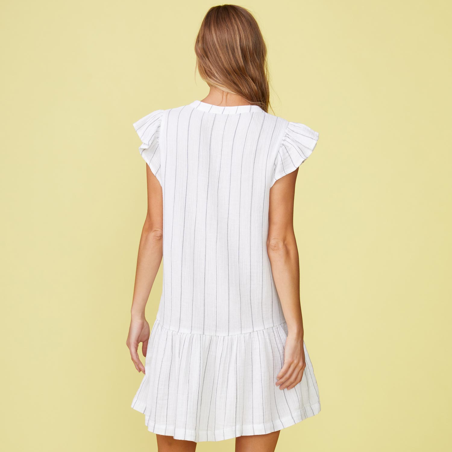 Back view of model wearing the pinstripe gauze easy ruffle dress in white.