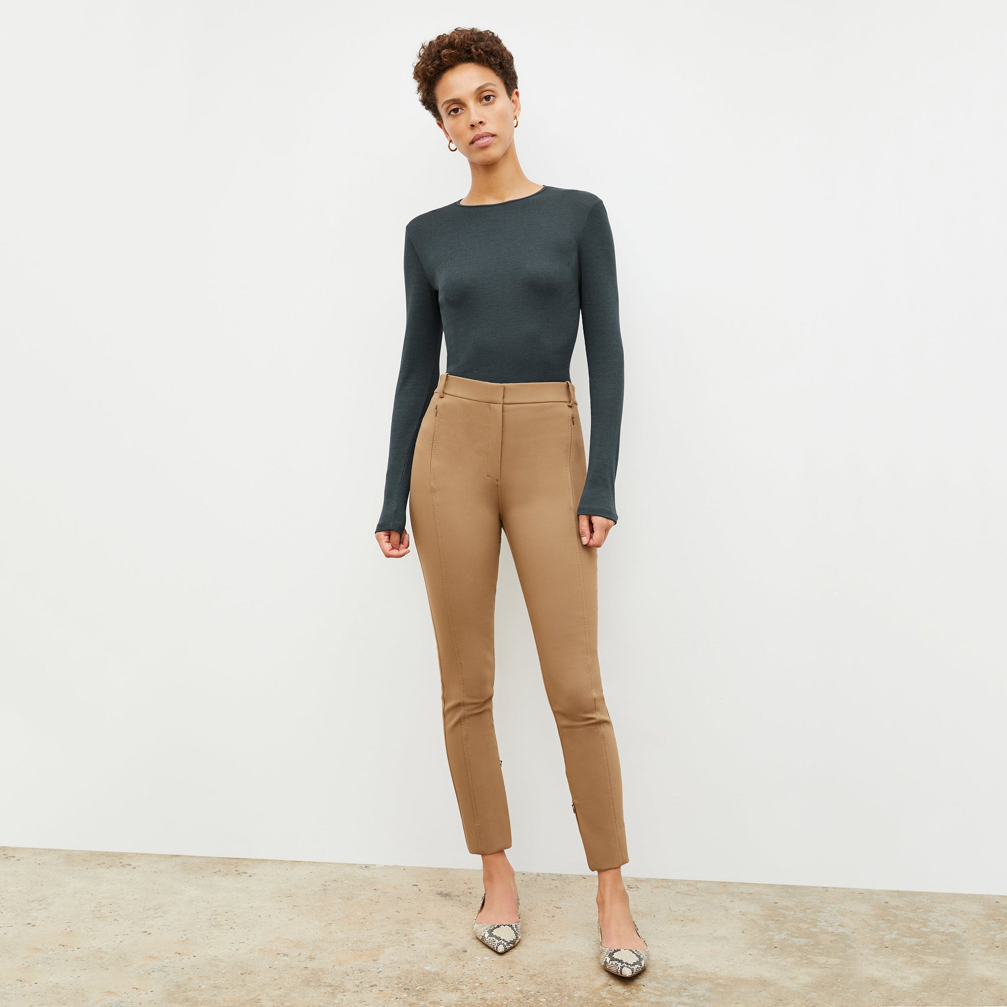 Front image of a woman standing wearing the Curie Pant—Everstretch in Saddle | Lead